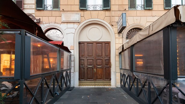 A narrow alleyway with a large wooden door at the end, flanked by glass enclosures with metal frames.