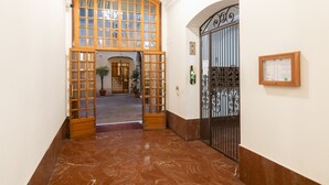 A hallway with a marble floor, a wooden door with glass panels, and a metal gate.