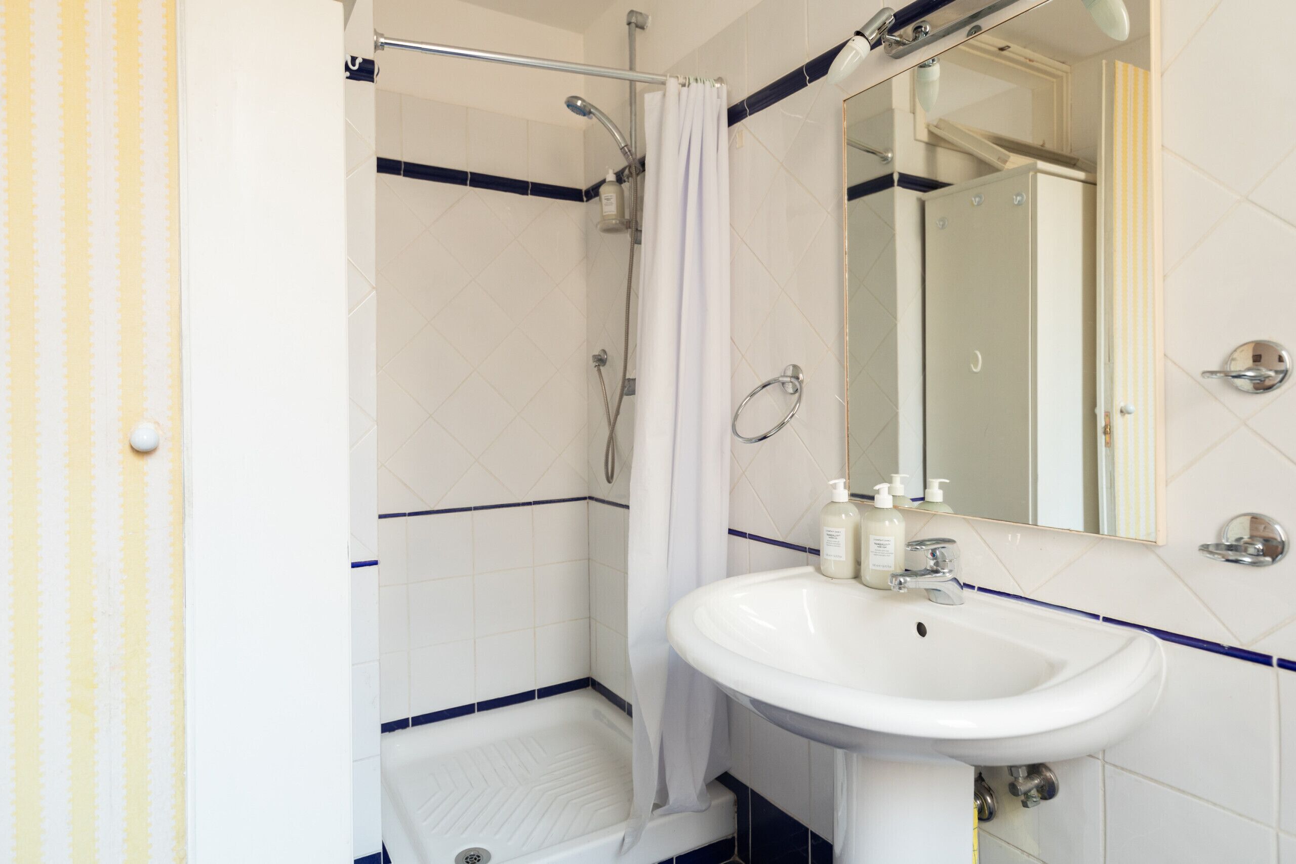 Een badkamer met een wit wastafelmeubel, een spiegel en een douche met gordijn.