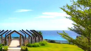 A modern building with a unique curved roof structure, a well-maintained lawn, and a view of the sea. - One Manchester Place 1BR Ocean View  (Lapu-Lapu)