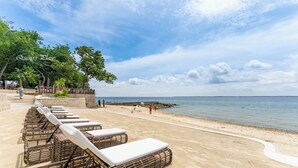 A beach with lounge chairs lined up along the shore, a wooden fence, and people walking. - One Manchester Place 1BR Ocean View  (Lapu-Lapu)