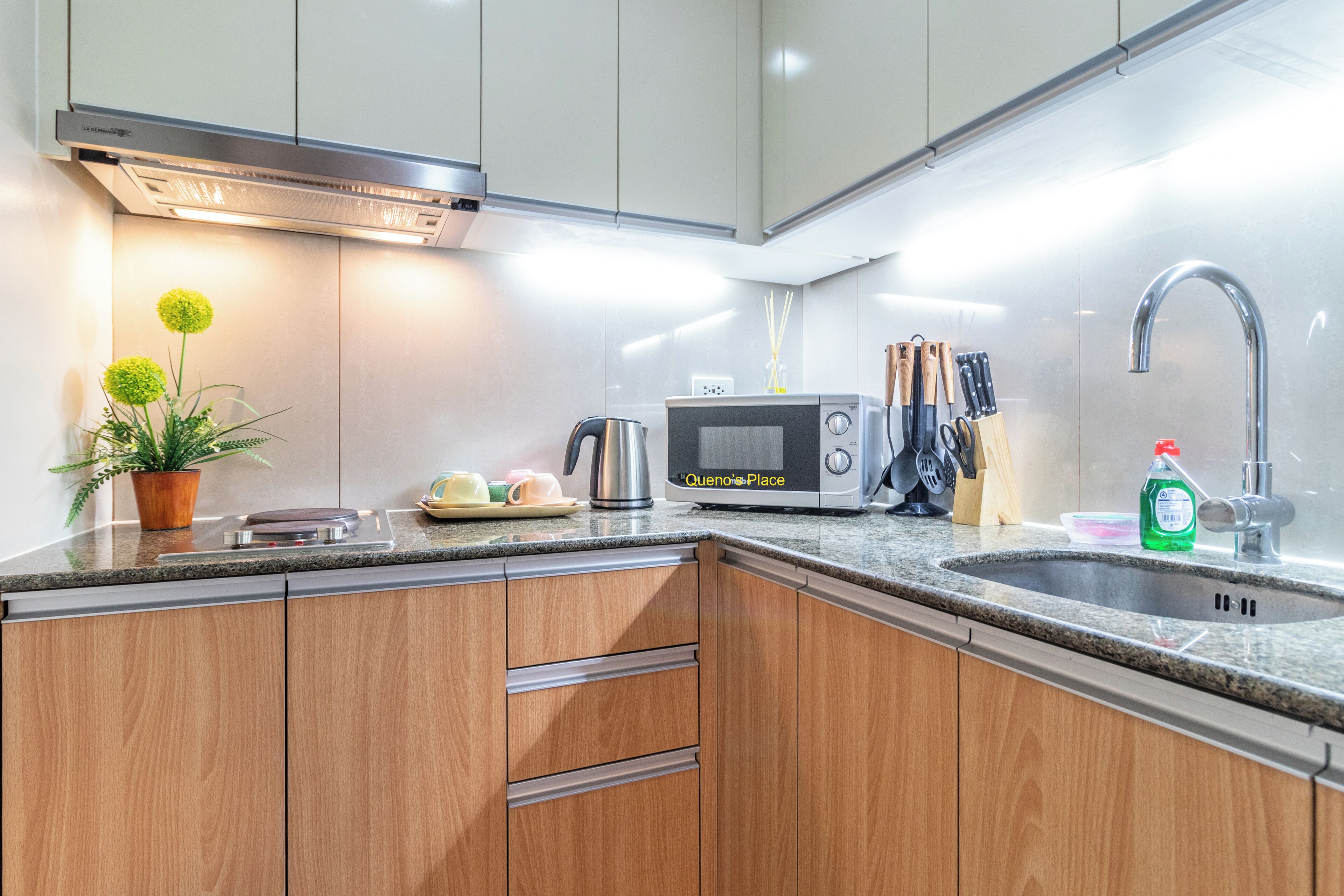 A modern kitchen with wooden cabinets, a stainless steel range hood, a microwave, and a sink.