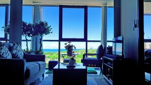 A living room with a large window, a sofa, a coffee table, and a television. - One Manchester Place 1BR Ocean View  (Lapu-Lapu)