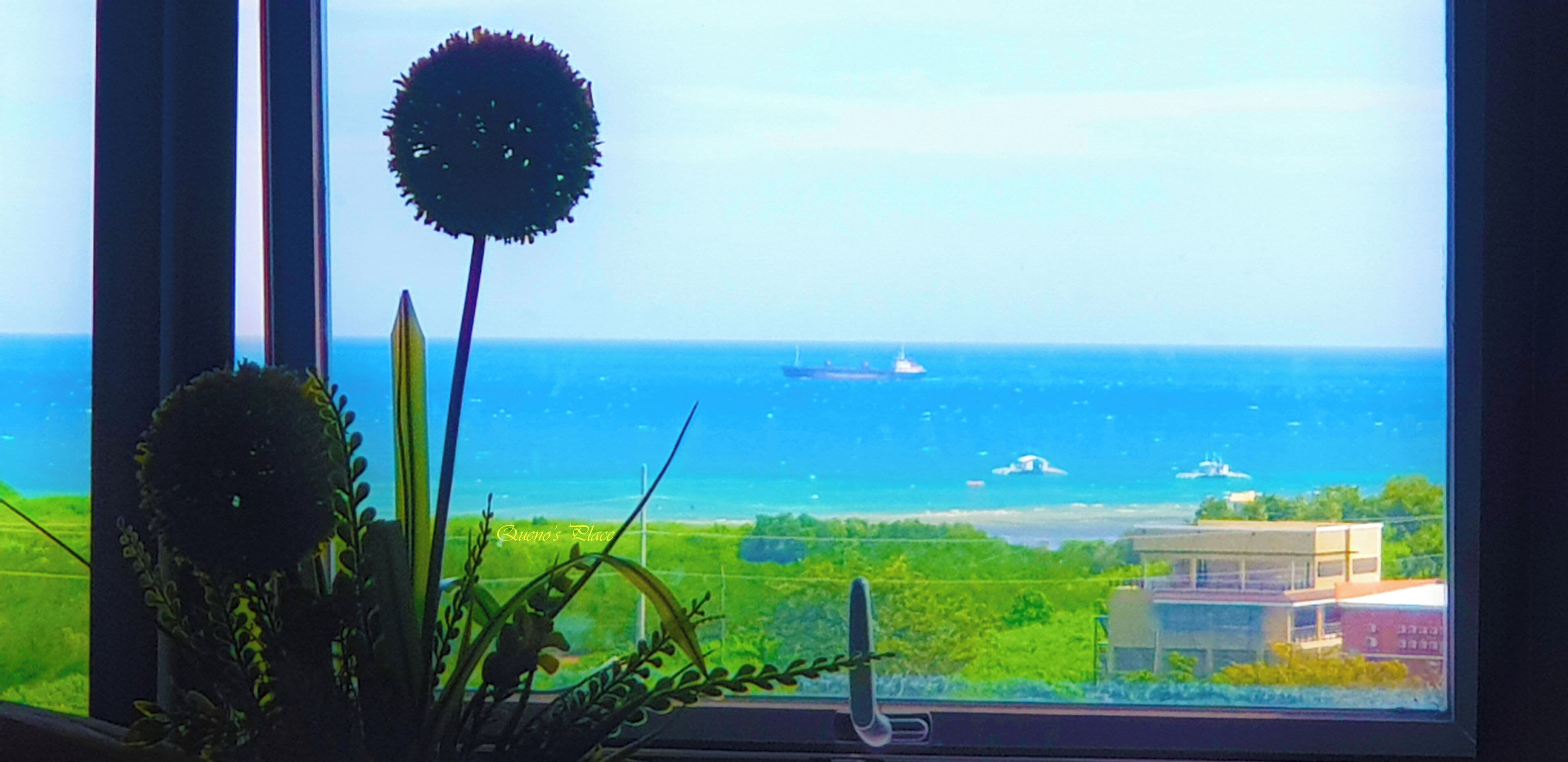 A view from a window overlooking a body of water with a ship and a building in the distance.