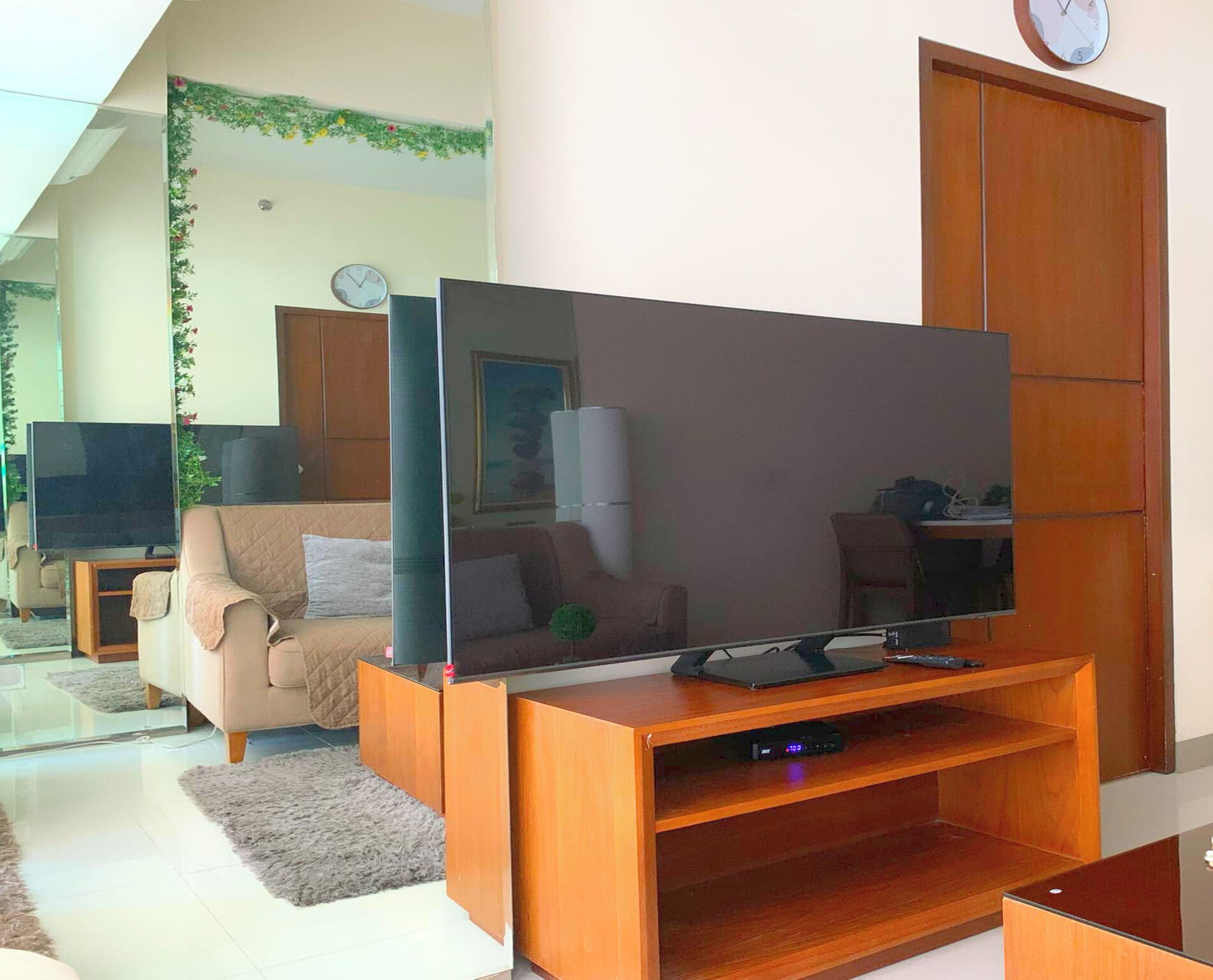 Una sala de estar con un televisor de pantalla plana sobre un soporte de madera, un sofá color beige, una mesa de centro y una puerta de madera.