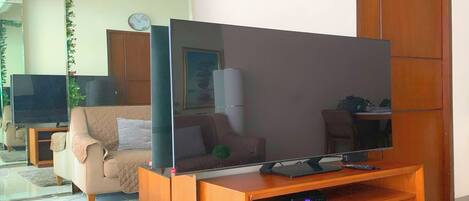 Una sala de estar con un televisor de pantalla plana sobre un soporte de madera, un sofá color beige, una mesa de centro y una puerta de madera.