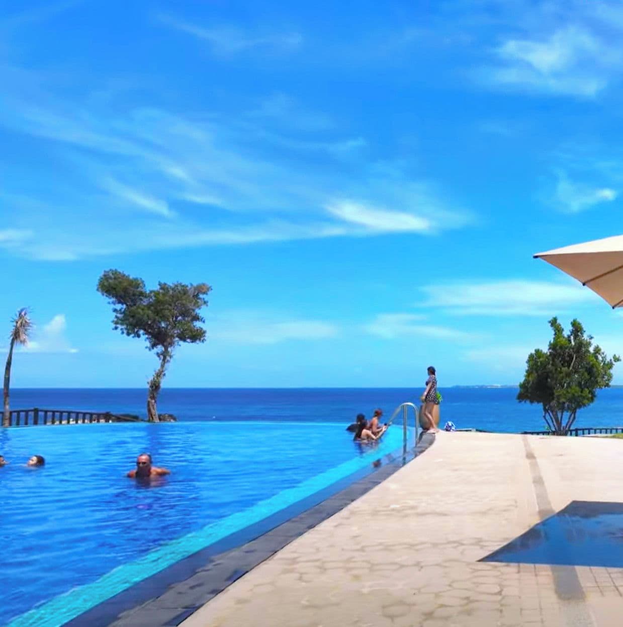 A swimming pool with clear blue water, surrounded by a tiled deck and palm trees.
