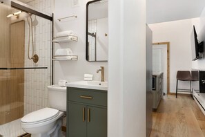 A modern bathroom with a glass shower enclosure, a toilet, a sink with a mirror, and a small seating area with chairs. - West Vail Matterhorn Condo - Steps to Bus (Vail)