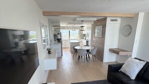 Ein modernes Wohnzimmer mit einer schwarzen Ledersofa, einem kleinen schwarzen Tisch und einem Essbereich mit einem runden Tisch und grauen Stühlen.