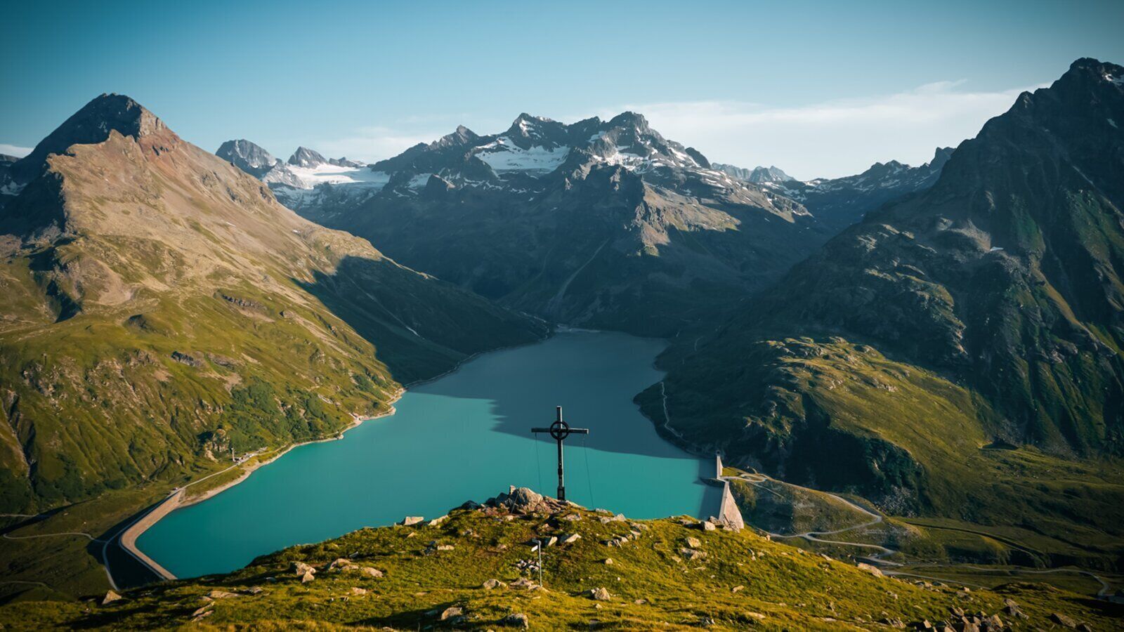 A mountain landscape with a lake and a cross structure in the foreground.