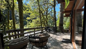 Una terraza de madera con dos mecedoras, rodeada de árboles y una valla de madera.