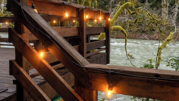 Una terraza de madera con barandilla que da a un río, rodeada de árboles y vegetación.