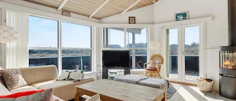 A spacious living room with a high ceiling, large windows, a fireplace, and a television.