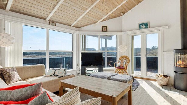 Ein geräumiges Wohnzimmer mit hoher Decke, großen Fenstern, einem Kamin und einem Fernseher.