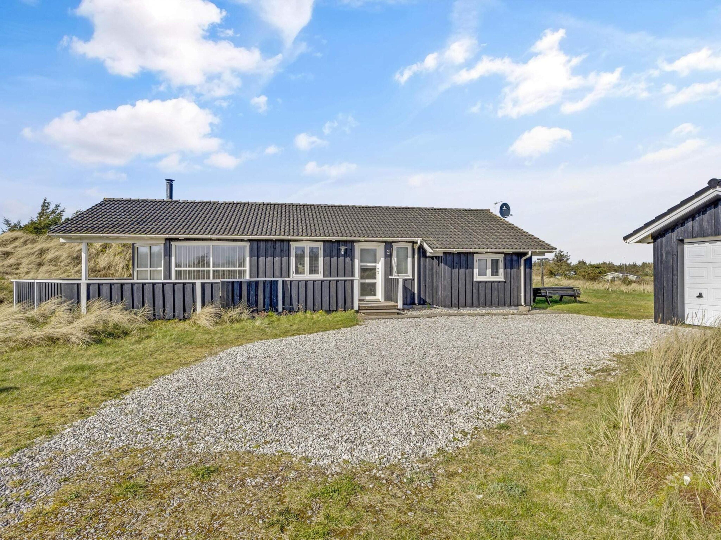 A two-story house with a gravel driveway, a wooden deck, and a garage.