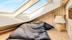 Ein Schlafzimmer mit Oberlicht, Holzwänden, einem Bett mit dunkler Bettwäsche und einer Nachttischlampe.