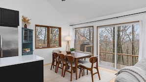 A modern kitchen with a dining area, large windows, and a view of trees.
