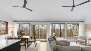 A spacious living room with a large sofa, dining area, and a view of trees through large windows.
