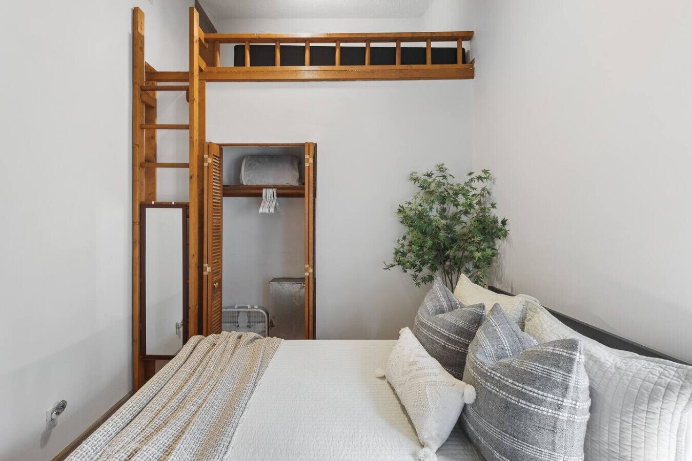 Une chambre avec un lit superposé, une échelle en bois, une petite armoire, un radiateur et une plante en pot.