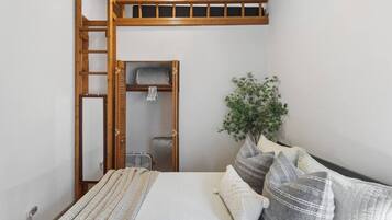 Une chambre avec un lit superposé, une échelle en bois, une petite armoire, un radiateur et une plante en pot.
