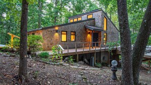 A modern wooden cabin with a deck, surrounded by trees.