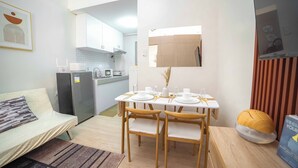 A compact living space with a dining table set for four, a sofa, a kitchenette, and a mirror.