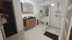 A modern bathroom with a glass shower enclosure, a wooden vanity, and a large mirror.