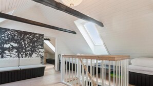 Ein Schlafzimmer im Loft-Stil mit Dachfenster, Holzbalken, einem weißen Babybett und einem Sofa.