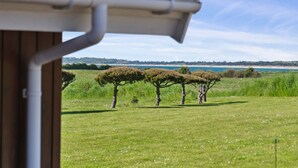 Blick auf eine Wiese mit drei Bäumen und einem Gewässer in der Ferne.
