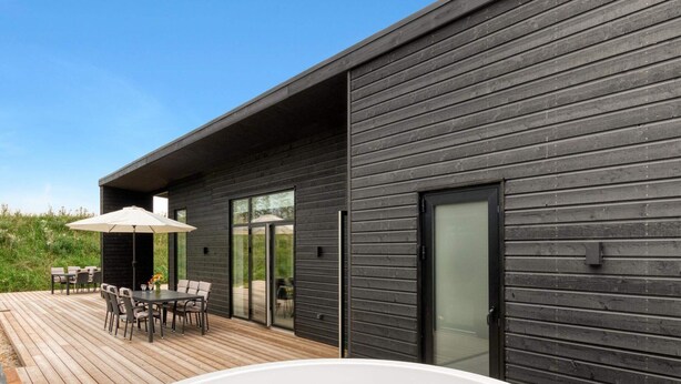 A modern outdoor deck with a hot tub, wooden furniture, and a glass door leading to an outdoor area. - 5 Star Holiday Home in Lokken (Lokken)