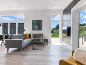 A modern living room with a grey sectional sofa, a coffee table, and a large window offering a view of the outdoors.