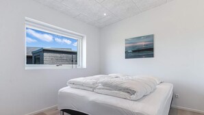 A bedroom with a bed, a window with a view of a building, and a painting on the wall. - 5 Star Holiday Home in Lokken (Lokken)