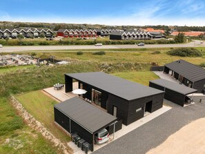 A modern building with a flat roof, a covered outdoor seating area, and a parking space with a car. - 5 Star Holiday Home in Lokken (Lokken)