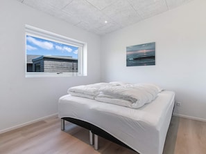 A bedroom with a bed, a window with a view of a building, and a painting on the wall.