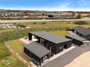 A modern building with a flat roof, a covered outdoor seating area, and a parking space with a car. - 5 Star Holiday Home in Lokken (Lokken)