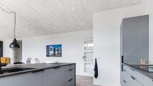A modern kitchen with grey cabinetry, a black pendant light, and a large island with a sink. - 5 Star Holiday Home in Lokken (Lokken)