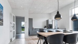 A modern kitchen with a central island, black chairs, and pendant lighting. - 5 Star Holiday Home in Lokken (Lokken)
