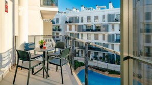 Un balcón con mesa y sillas, con vista a una piscina y edificios cercanos.