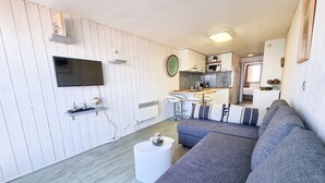A modern living room with a grey sofa, a flat-screen TV, and a kitchen area with a dining table and bar stools. - [Vue Imprenable] Appartement Rénové Front de Mer (Arcachon)