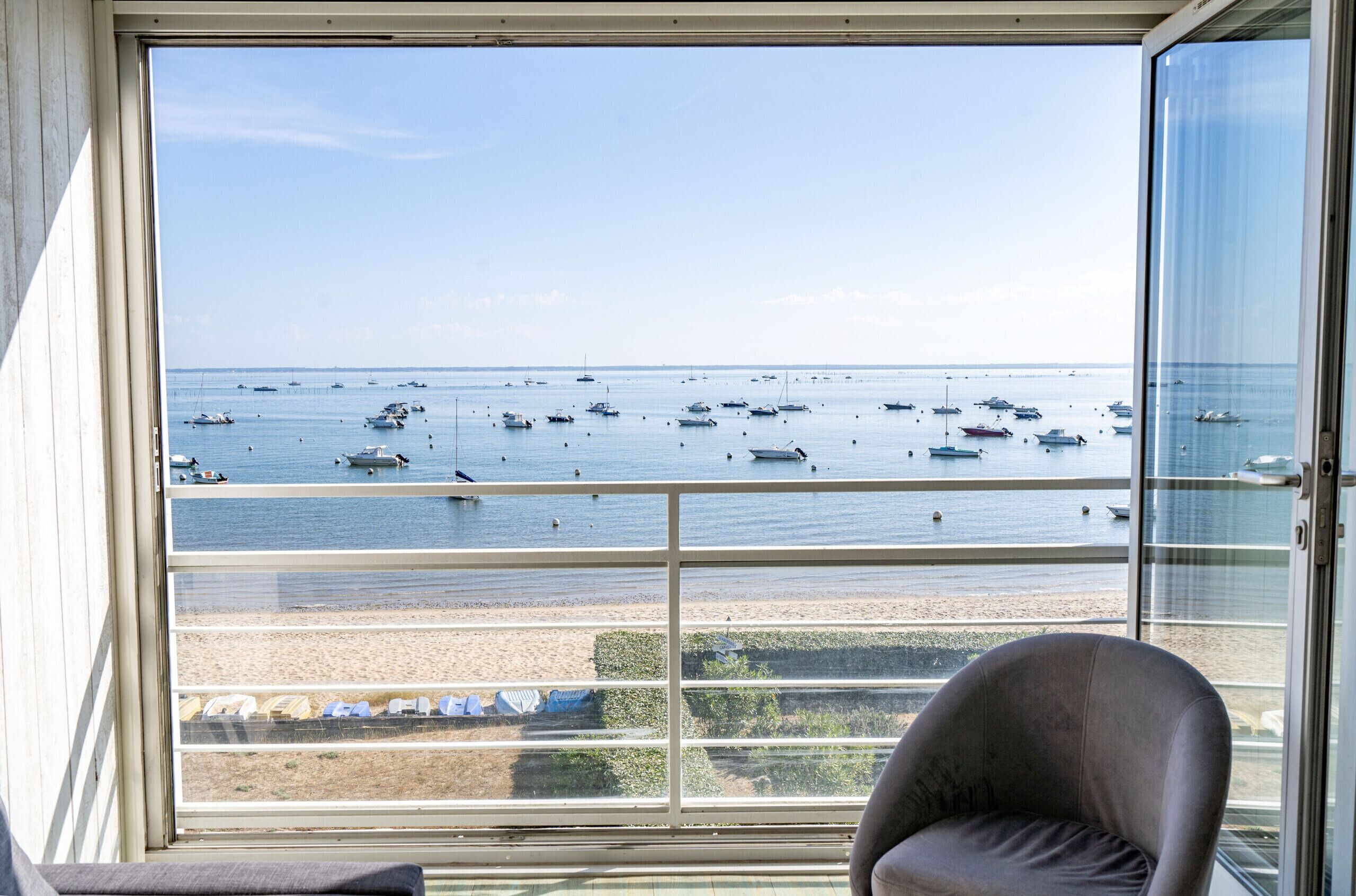 Una habitación con un amplio ventanal que da a una playa con barcos.