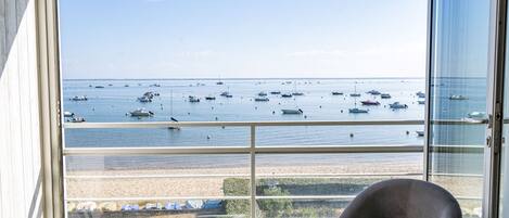 Una habitación con un amplio ventanal que da a una playa con barcos.