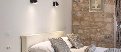 A bedroom with a stone wall, a bed with patterned pillows, a nightstand, and wall-mounted lights.