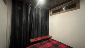 A bedroom with a bed, a wooden bench, a window, and a curtain.