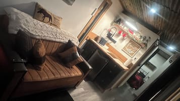 A cozy living room with a brown sofa, a coffee table, and a dining area with a kitchen counter and refrigerator.