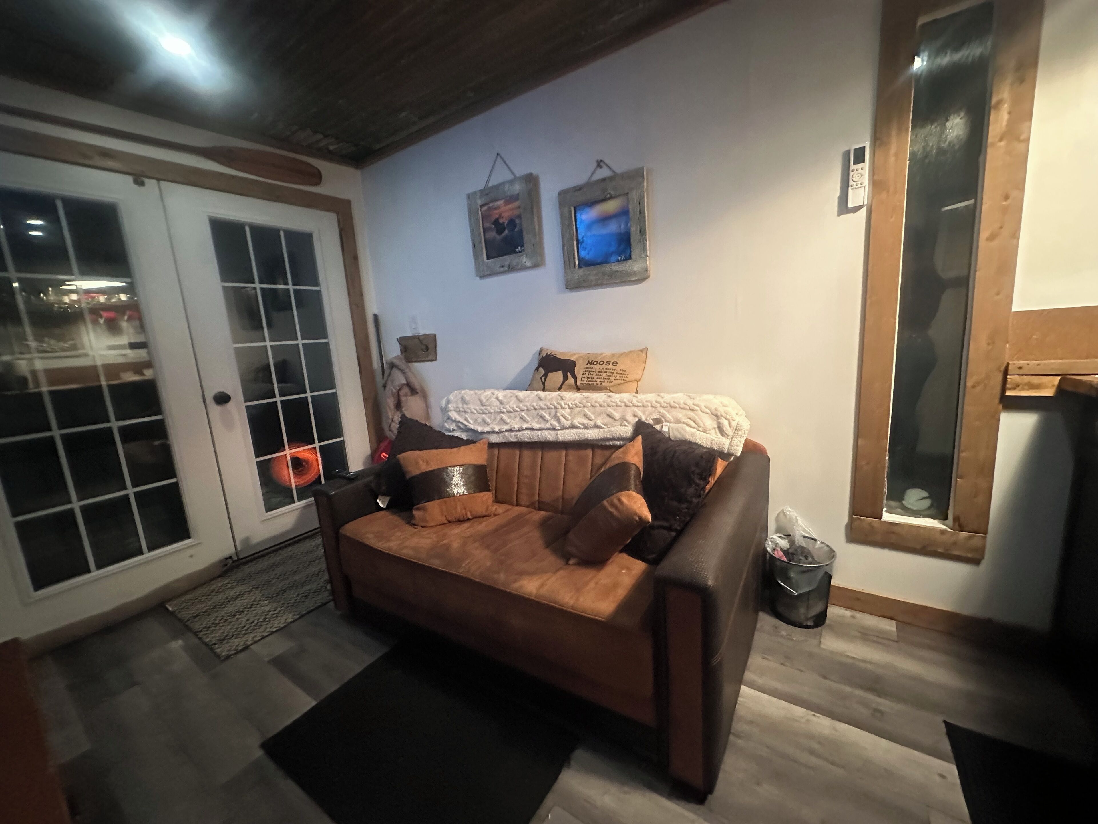 A cozy living room with a brown leather sofa, a white blanket, and a framed picture of a moose on the wall.