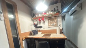A compact kitchen with a wooden countertop, a coffee maker, a kettle, and a paper towel holder. There is a small sink and a cabinet below the countertop.