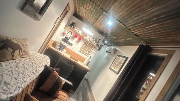 A cozy living room with a brown sofa, a coffee table, and a TV. There's a kitchen area with a fridge and a sink in the background.