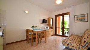 A small, cozy room with a wooden table, chairs, a sofa, a TV, and a window with a view of greenery. - Fun and cozy retreat with shared swimming pool (Bibione)