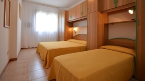 Habitació d'hotel amb dos llits individuals, un armari de fusta, un mirall i una finestra amb cortines.