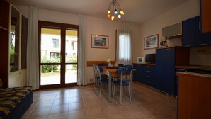 Una habitación con cama, una mesa de comedor con sillas, kitchenette y un ventanal con vistas a un edificio.